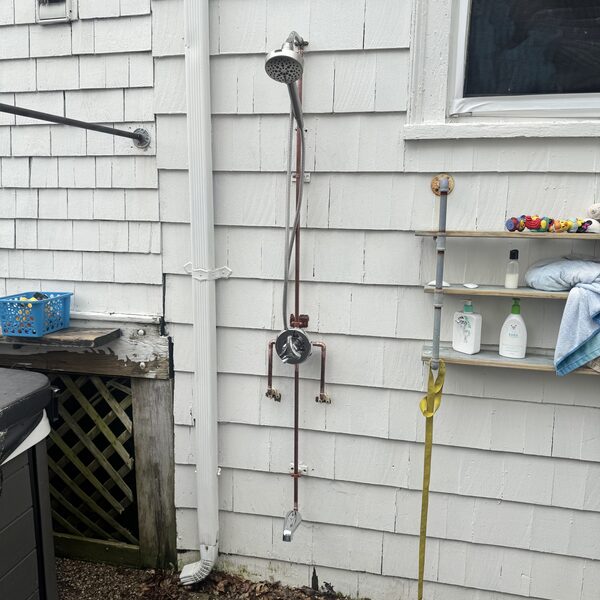 Custom copper outdoor shower installed on cedar-shingle siding with a showerhead, mixing valve, and lower foot-rinse spigot